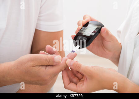 Medico utilizzando glucometro sul dito del paziente Foto Stock