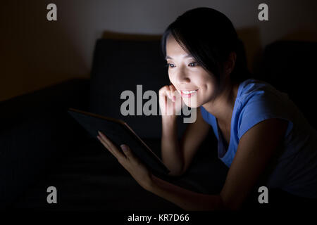 Donna asiatica con tavoletta digitale e giacente sul letto Foto Stock