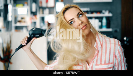 Sorridente giovane donna soffiare i capelli di essiccazione Foto Stock