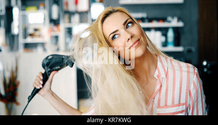 Sorridente giovane donna soffiare i capelli di essiccazione Foto Stock