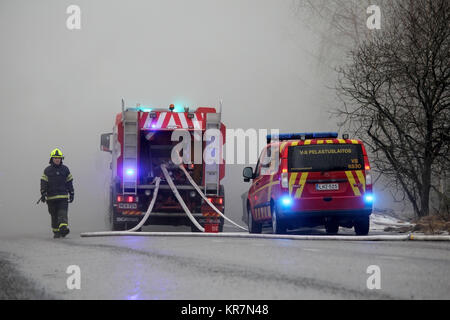 SALO, Finlandia - 16 febbraio 2014: pompiere emerge dal fumo pesante al fuoco scena di Salo impianto di cemento, con due camion fuoco sulla strada. Foto Stock