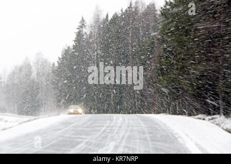 Auto guidando lungo una strada rurale durante una bufera di neve. Foto Stock