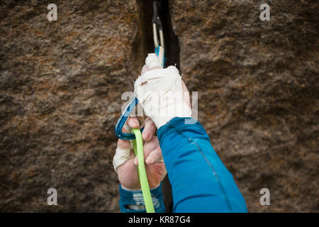 Dettaglio di un uomo clipping nella sua fune ad una di quickdraw durante una arrampicata Foto Stock