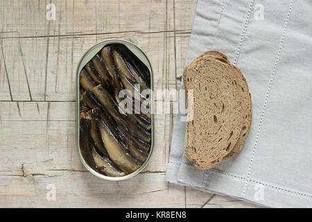 Barattolo di latta di spratti Sardine, con pezzi di pane su un tavolo di legno. Vista superiore e spazio libero. Messa a fuoco selettiva. Foto Stock