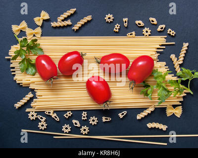 Spaghetti con pomodori verdi e altri figurato di pasta a forma di prua, spirali, figure di razzi e stelle per la cottura su uno sfondo scuro Foto Stock