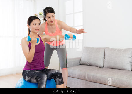 Attraente bellezza studentessa seduti sulla sfera di yoga e tenendo il manubrio rendendo il pugilato gesto corpo di allenamento con la sua casa fitness teacher. Foto Stock