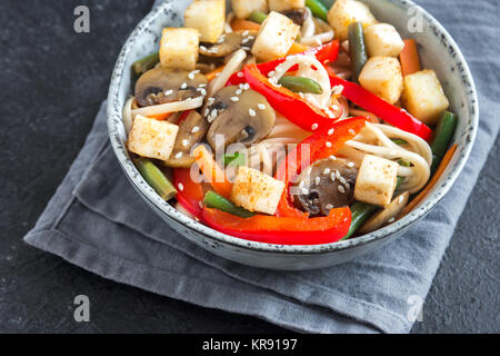 Stir fry con udon noodles, tofu, funghi e ortaggi. Asian vegane cibo vegetariano, pasto, STIR FRY su sfondo nero vicino. Foto Stock