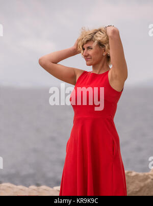 Bella donna in abito rosso in prossimità del mare Foto Stock