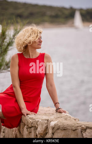 Ricci bella ragazza bionda in abito rosso in prossimità del mare Foto Stock