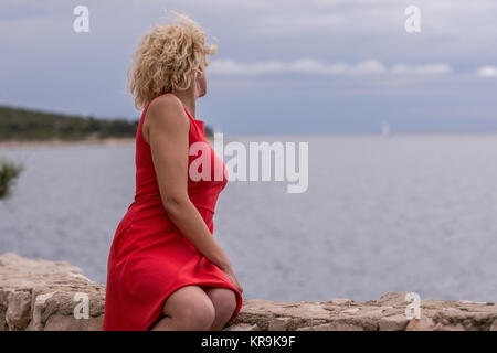 Ricci bella ragazza bionda in abito rosso in prossimità del mare Foto Stock