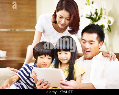 Asian genitori la madre e il padre e i due figli del figlio e figlia seduti sulla famiglia del lettino con tavoletta digitale insieme. Foto Stock