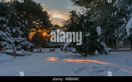 Il sole splende attraverso gli alberi sul cimitero nevoso in Great Malvern Priory e Malvern, Worcestershire, Regno Unito Foto Stock