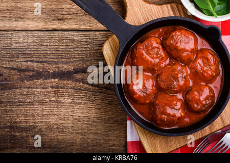 Polpette di carne in padella in ghisa con salsa di pomodoro servito fresco con insalata di spinaci su tavola in legno rustico, vista dall'alto Foto Stock