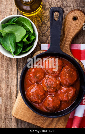 Polpette di carne in padella in ghisa con salsa di pomodoro servito fresco con insalata di spinaci su tavola in legno rustico, vista dall'alto Foto Stock