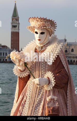 Il Carnevale di Venezia 2017, Veneto, Italia donna in un intricato costume classico nell'ultimo albero di luce del sole al tramonto con la laguna e campanile behi Foto Stock