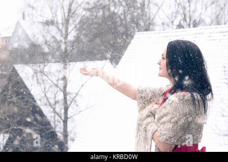 Bruna giovane ragazza in un abito rosso e coperto con un handmade scialle gode della nevicata e le catture di fiocchi di neve con la sua mano. Foto Stock