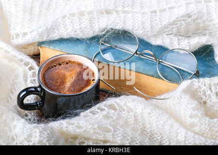 Una tazza di caffè avvolto in una sciarpa, maglione o caldi plaid, con un libro e occhiali. In autunno o inverno, fine settimana, vacanza o di mattina di buon concetto. Clos Foto Stock