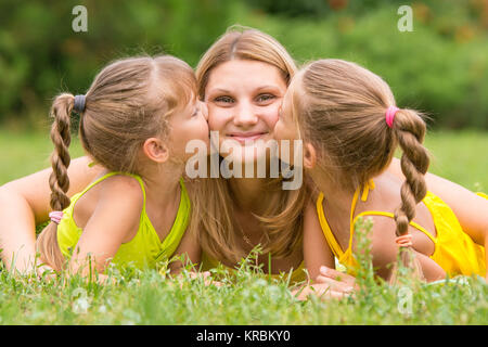 Due figlie kissing madre sdraiati sull'erba su un picnic Foto Stock