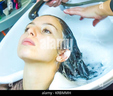 Donna capelli di lavaggio nel salone di parrucchiere con testa indietro nel dissipatore avente peli bagnati e avvolto in shampoo schiuma Foto Stock