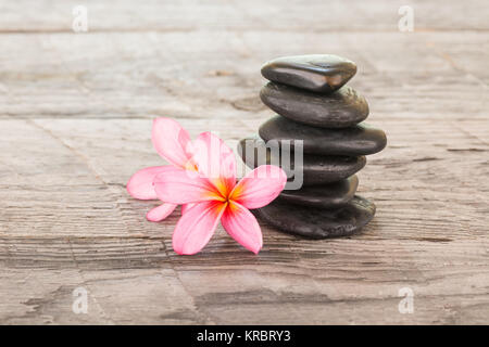 Plumeria fiori e pietre nere su legno stagionato Foto Stock