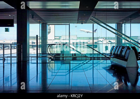 Svuotare airport lounge di partenza con posti a sedere e scale mobili che si affaccia sulla pista con un piano di attesa. Foto Stock