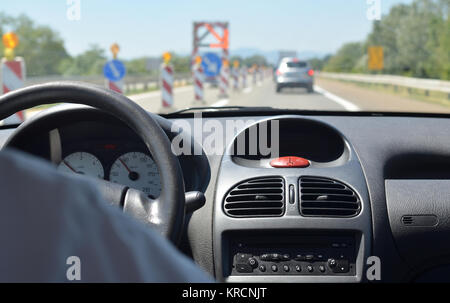 Alla guida di una vettura su una autostrada con cantieri stradali e con altri veicoli sfocato davanti a lui Foto Stock