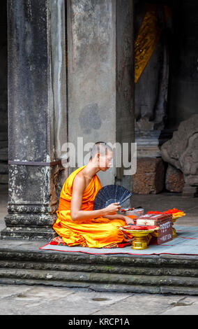 Giovane monaco buddista in abiti dello zafferano si siede in Angkor Wat, un tempio complesso vicino a Siem Reap in Cambogia, il più grande monumento religioso nel mondo Foto Stock