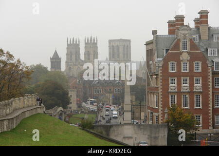 Vista della cattedrale di York in una giornata grigia. La costruzione è iniziata nel 1220 -- è una delle più grandi cattedrali gotiche del nord Europa, ed è la sede dell'Arcivescovo di York. La gente può essere vista sulla sinistra, camminando lungo le antiche mura della città. Foto Stock