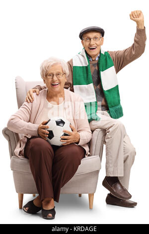 Allegro anziani appassionati di calcio con un campo di calcio e un foulard seduto in poltrona isolati su sfondo bianco Foto Stock