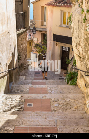 Donna passeggiando per le ripide scale di ciottoli nel borgo medievale di Eze, Cote d'Azur, in Francia Foto Stock