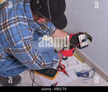 Il tecnico indossa i normali dispositivi di protezione. Per elettricista mani assembla un bipolare standard di presa di corrente a muro. Foto Stock