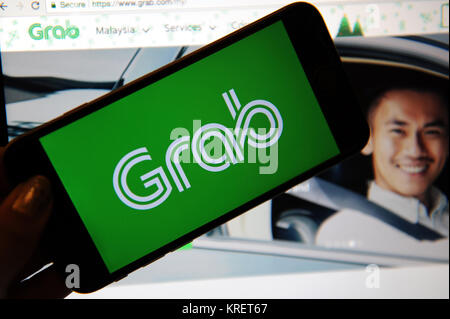 Grab, il viaggio salutando il logo della società su un telefono e sito web sullo schermo di un computer Foto Stock