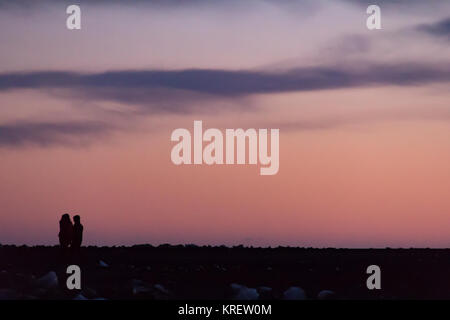 Due persone che camminano attraverso un paesaggio roccioso in silhouette contro un cielo colorfuly al tramonto Foto Stock