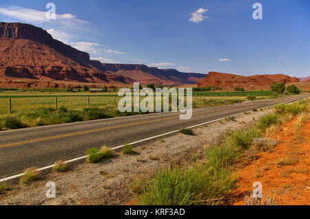 Strada nel deserto con fertili irrigate verde dei terreni agricoli e di enorme red mesa in background Foto Stock