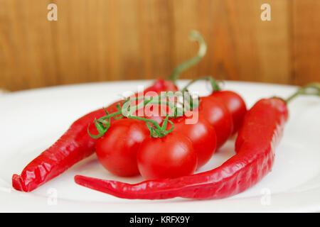 Rossi pomodori ciliegini e due cialde di peperoncino piccante Foto Stock