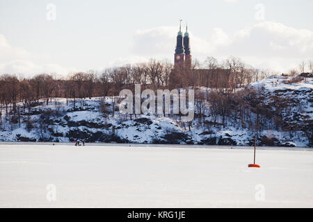 Pesca sul ghiaccio sulla congelati Riddarfjärden, Mälaren. Lo sfondo è il Långholmen island e la chiesa Högalid da Södermalm isola Foto Stock