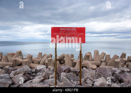 Avviso di pericolo di segno per la difesa del mare struttura superficiale irregolare. Non salire sulla o sulle rocce vicino a Llanddulas North Wales UK Foto Stock