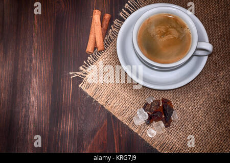 White tazza di caffè e lo zucchero di canna e la cannella in un marrone tavolo in legno Foto Stock