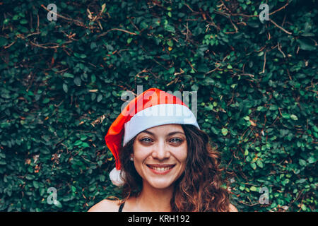 Giovane bella donna sorridente, indossando un cappello di Natale, su uno sfondo verde Foto Stock