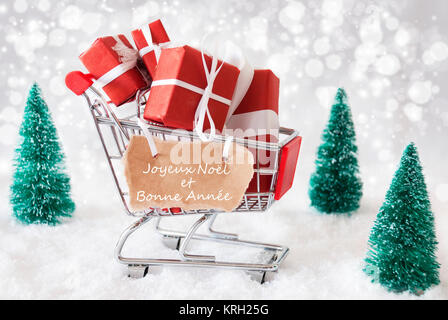 Trollye con regali di Natale o regali. Scenario innevato con neve e alberi. Vini spumanti Bokeh effetto. Etichetta con testo francese Joyeux Noel et bonne Annee significa Buon Natale e Felice Anno Nuovo Foto Stock