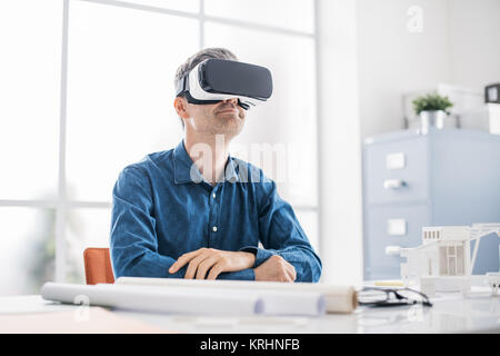 Architetto professionista lavorando in ufficio e di indossare un auricolare VR, egli è la visualizzazione di una virtual reality interface Foto Stock