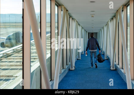 Un uomo con uno zaino nelle sue mani passeggiate lungo il corridoio a bordo del piano. Fuori dalla finestra la parte di alimentazione del velivolo. Foto Stock