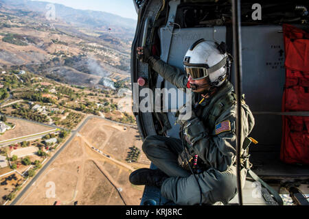 Naval Aircrewman (elicottero) 1a classe Justin Greene assegnato al "Merlin" di elicottero di mare squadrone di combattimento (HSC) 3 ricerche per gli hotspot da un MH-60S Sea Hawk elicottero per supportare la California per la lotta antincendio sforzi. HSC-3 e HSC-21 assistono California Dipartimento di silvicoltura e protezione antincendio fornendo personale di volo battenti appositamente attrezzate MH-60S elicotteri per condurre una antenna di gocce di acqua contro incendi in San Diego County. (U.S. Navy Foto Stock