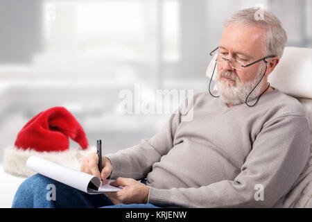 Il vecchio uomo che fa un elenco di acquisti con carta e penna per vacanze vicino a un Red Hat Foto Stock