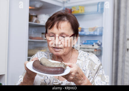 Felice donna senior tenendo la piastra con salsicce di fegato di maiale Foto Stock