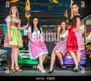 Giovani e donne attraenti al Oktoberfest con tradizionale Dirndl vestiti, autoscooter in background Foto Stock