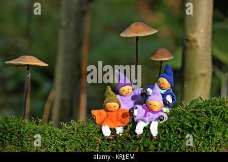 quattro gnomi sono seduti nel muschio sotto i funghi Foto Stock