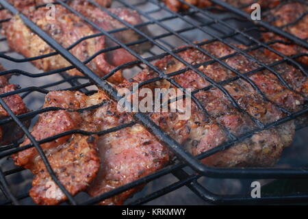 Su una buona giornata estiva, persone a cuocere la carne su un barbecue. La carne è quasi pronto, è già rosolato e coperto con una sottile crosta deliziosa. Foto Stock