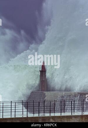 Onda di tempesta oltre il vecchio faro e il molo di Viavelez nelle Asturie, Spagna. Foto Stock