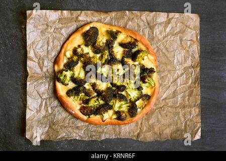 Pizza con broccoli e formaggio su carta su sfondo scuro. Vista superiore, laici piatta Foto Stock
